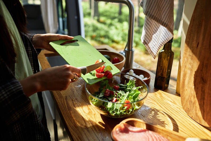 Préparation d'une salade fraîche dans un van aménagé avec planche à découper et légumes, vue sur la nature