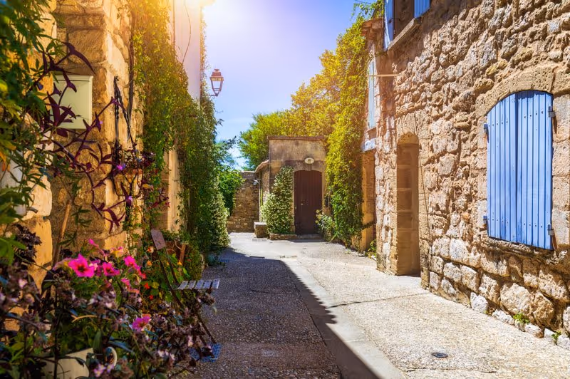 Ruelle en pierre à Venasque en Provence avec maisons anciennes, volets bleus et fleurs