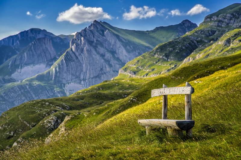 Vue sur Bobotov Kuk, le point culminant du Durmitor au Monténégro, avec un banc en bois rustique au premier plan sur les pentes verdoyantes