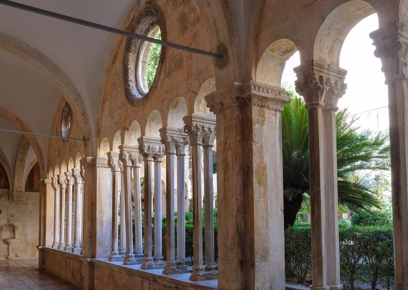 Cloître gothique du monastère franciscain de Dubrovnik avec ses colonnes de pierre finement sculptées et son jardin intérieur verdoyant, datant du XIVe siècle