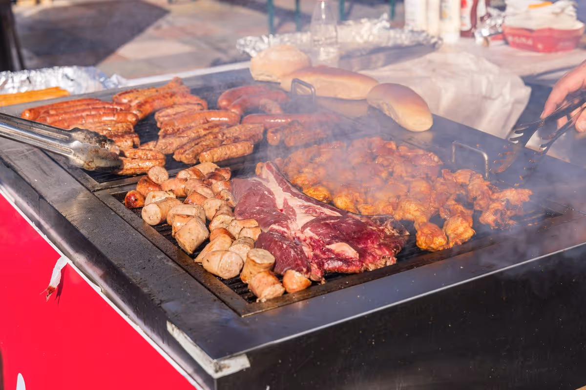 Barbecue extérieur à Tirana en Albanie avec saucisses grillées, brochettes, pièce de bœuf et morceaux de poulet marinés sur une grande plancha fumante