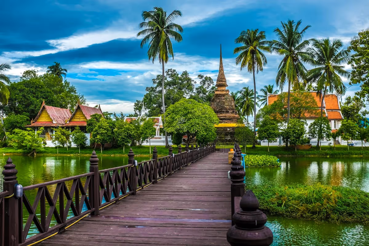 Temple bouddhiste entouré de palmiers en Thaïlande, accessible par une passerelle en bois sur l'eau