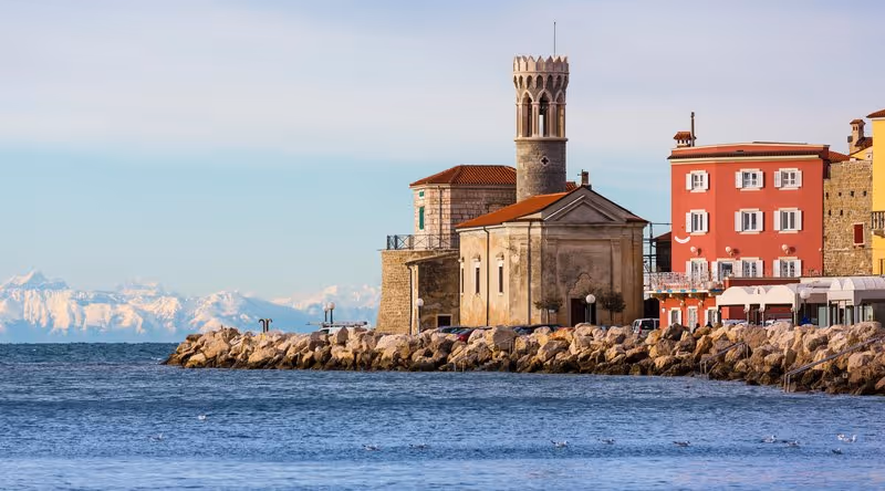 Phare et église au bord de mer à Piran avec les Alpes enneigées en arrière-plan