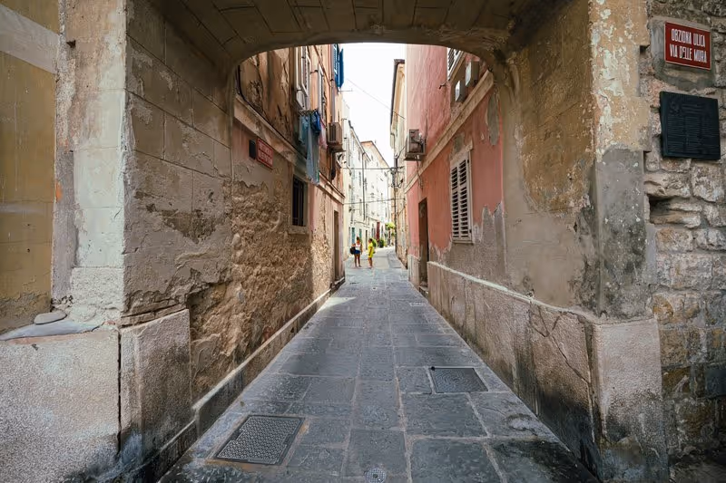 Ruelle pavée du centre historique de Piran avec arche en pierre et façades colorées, Slovénie