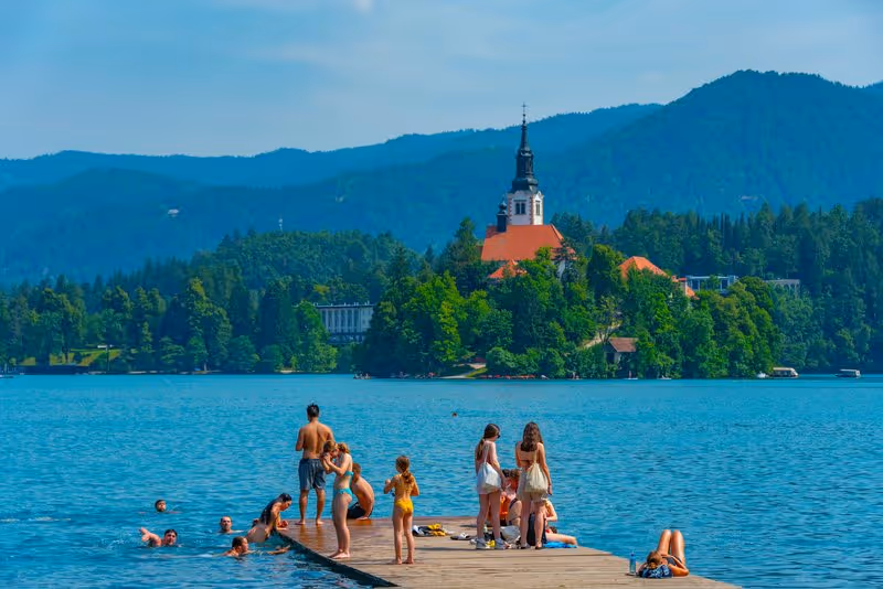 Lac Bled en Slovénie – baigneurs sur un ponton avec l'île et l'église de l'Assomption en arrière-plan
