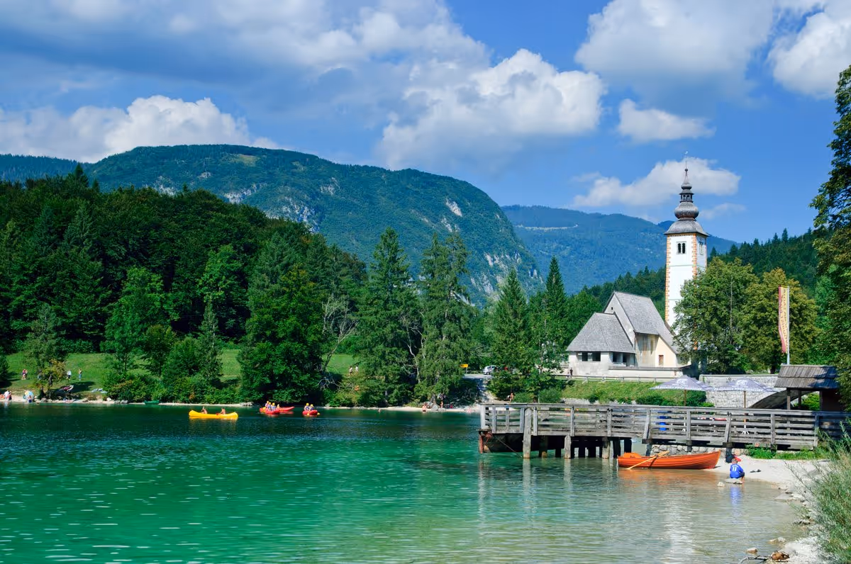 Lac de Bohinj en Slovénie avec ses eaux turquoise, des kayaks colorés et l'église Saint-Jean-Baptiste en arrière-plan