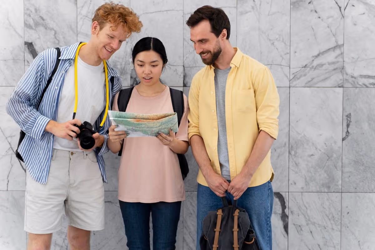 Trois voyageurs consultant une carte routière pour organiser leur road trip, avec appareil photo et sac à dos