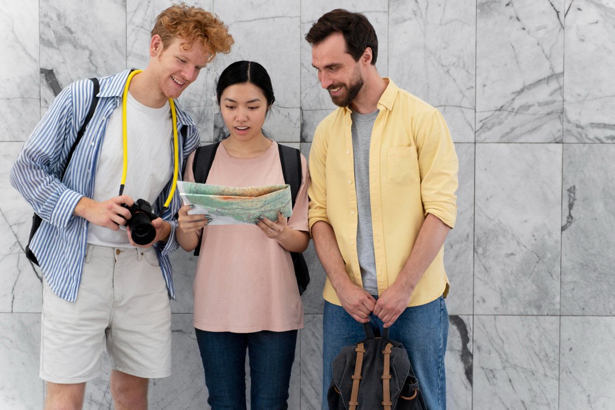 Trois voyageurs consultant une carte routière pour organiser leur road trip, avec appareil photo et sac à dos