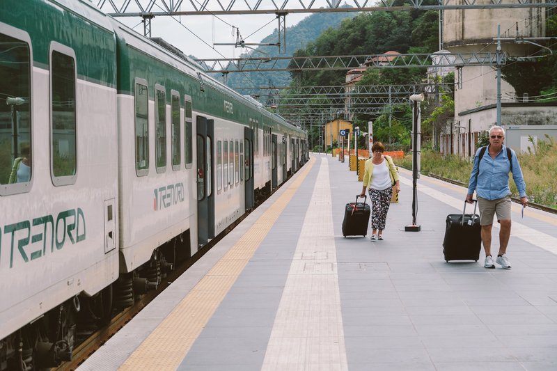 Des voyageurs avec leurs valises sur le quai d'une gare italienne, longeant un train régional Trenord vert et blanc