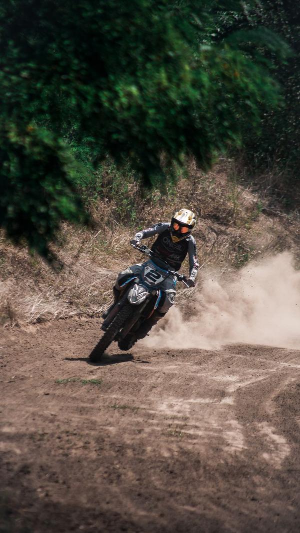 Pilote de moto tout-terrain en pleine accélération sur une piste de terre à Bali, gerbe de poussière derrière la roue arrière