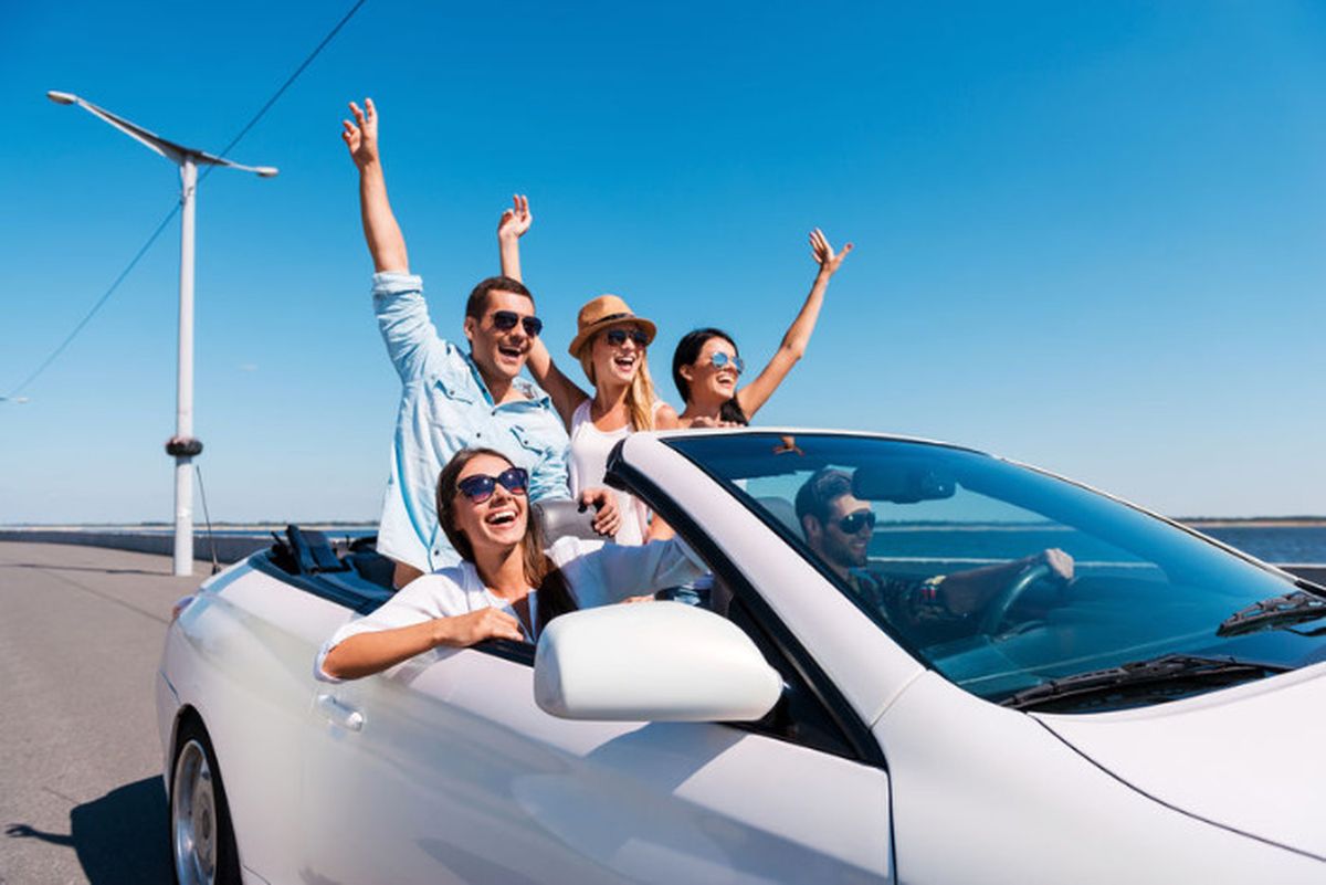 Groupe d'amis heureux en road trip dans une voiture décapotable blanche, bras levés au soleil