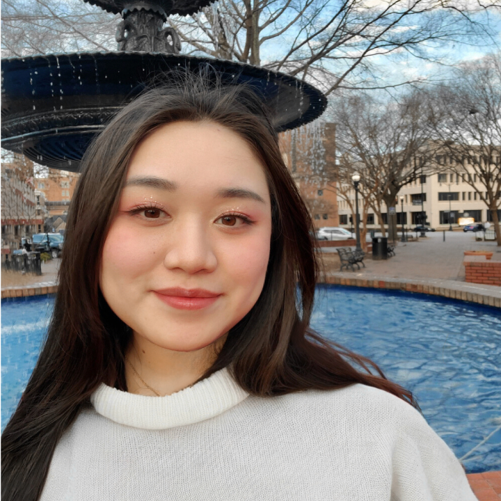 Woman wearing a white sweater in front of a fountain/