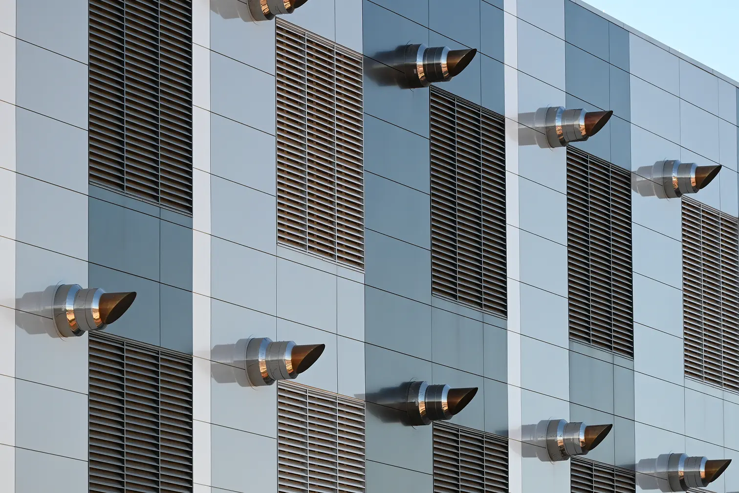 Side of a modern building featuring multiple ventilation grilles and protruding metal exhaust vents.