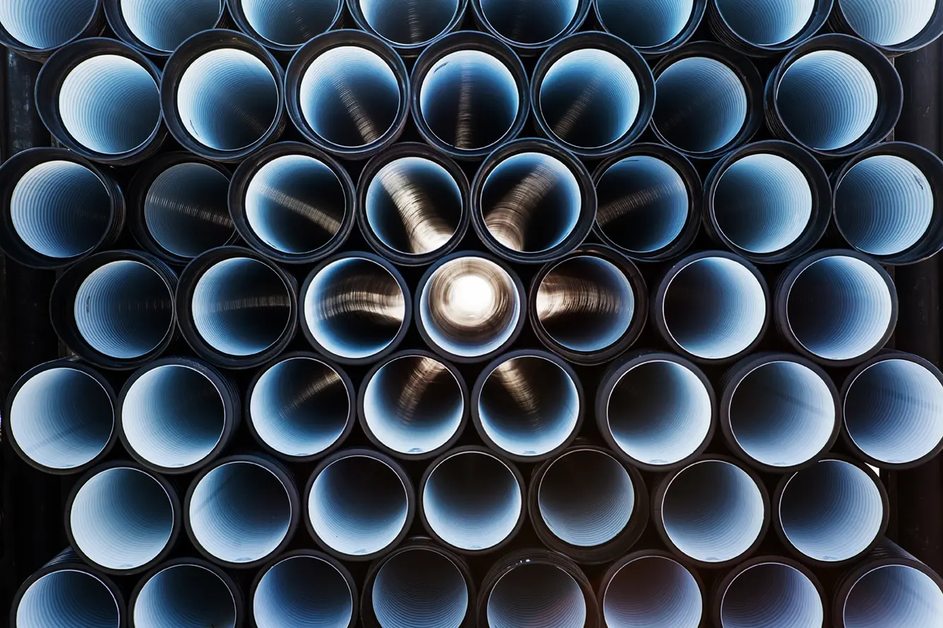 Top-down view of stacked industrial metal pipes arranged in a circular pattern with light reflecting inside.