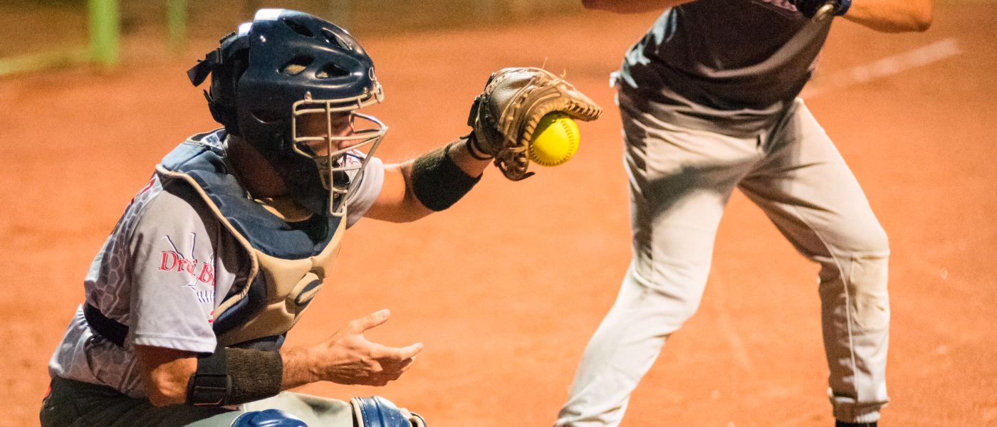Catcher in a softball game wearing wrist guard catching a ball mid-play, illustrating wrist hyperextension. A common motion that can contribute to dorsal intercalated segment instability (DISI) due to repetitive stress on the scapholunate ligament.