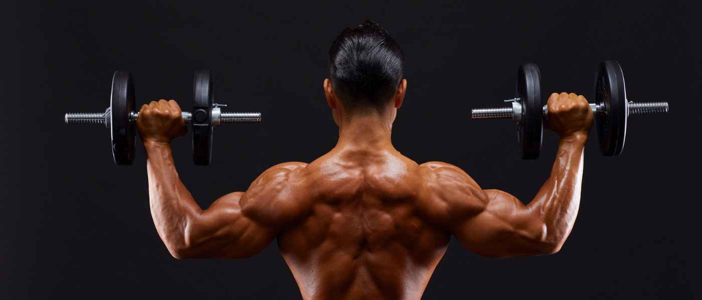 "Back view of a muscular man lifting dumbbells during a workout, showing muscle definition and strength training related to delayed onset muscle soreness and recovery"