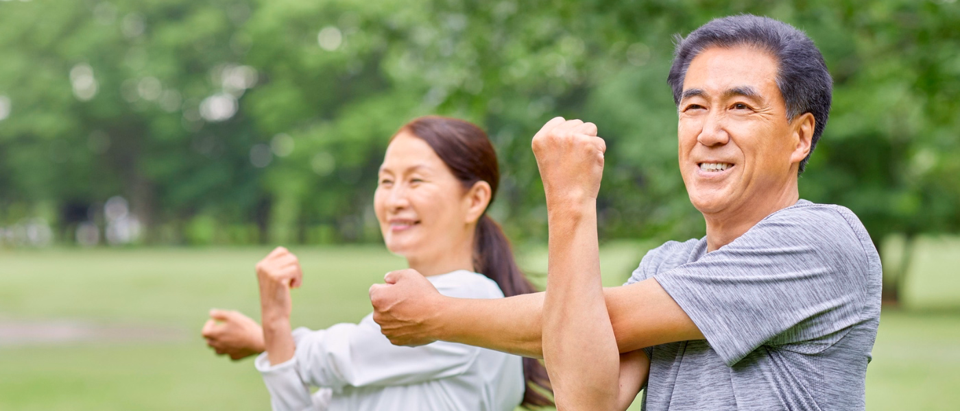 Older man and woman stretching outdoors in a park, demonstrating gentle shoulder mobility exercises after arthroscopic labrum repair surgery