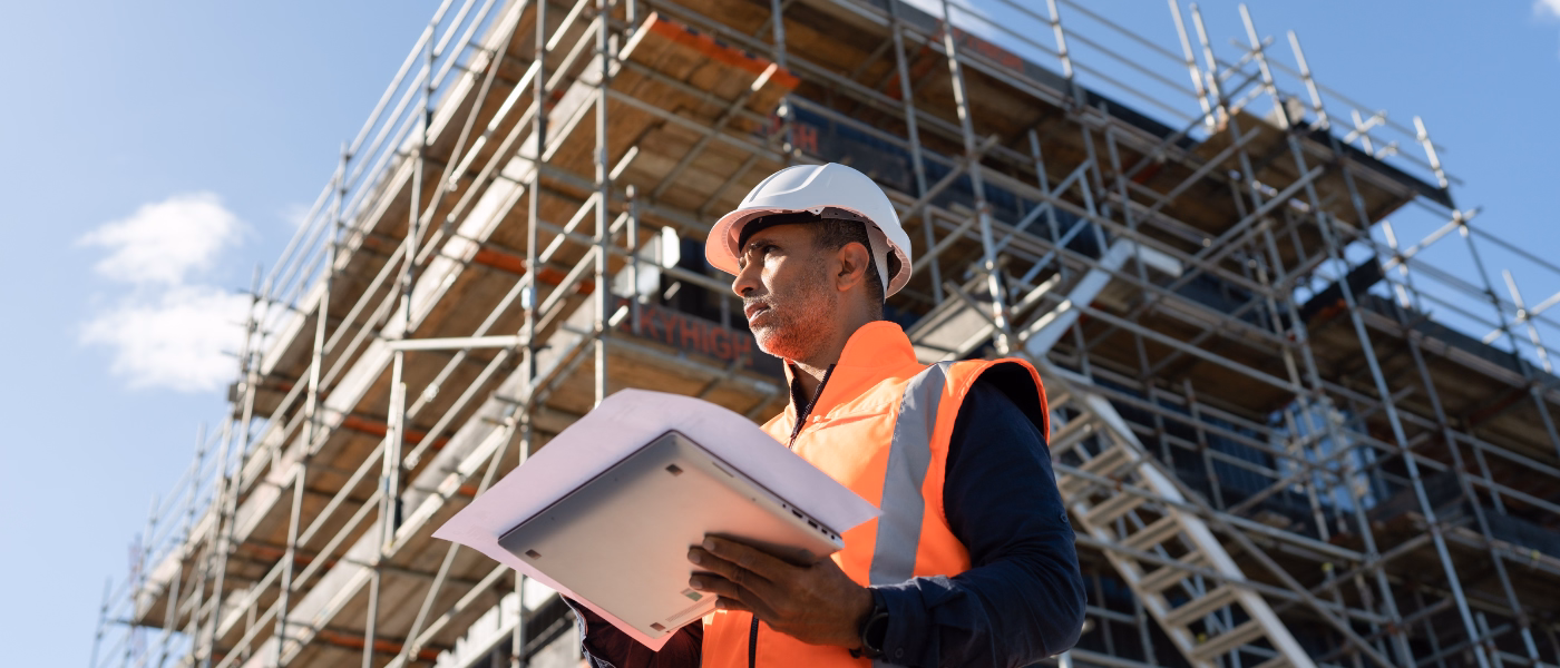 Construction worker in safety gear holding documents on a building site, symbolizing occupational risks linked to Myofascial Pain Syndrome (MPS) due to repetitive strain and physical labor.