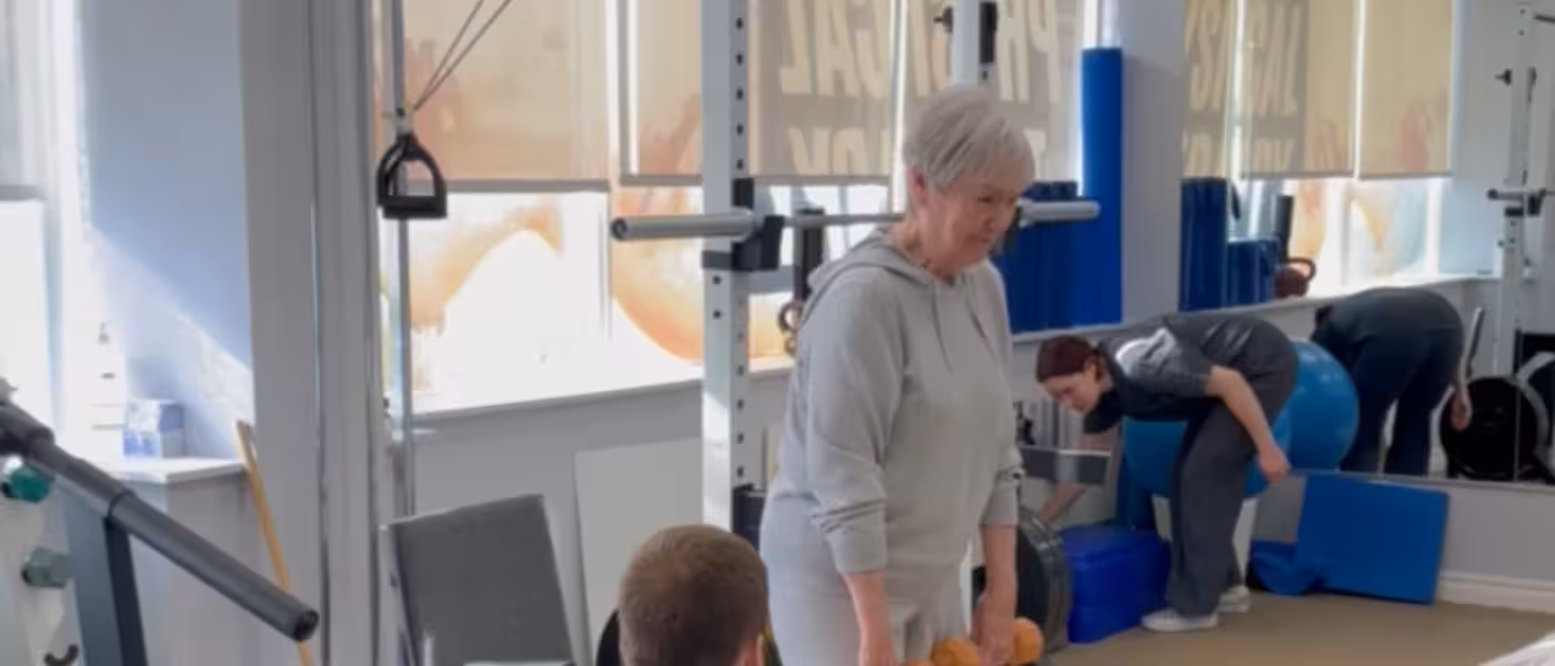 Older adult performing supervised strength training with dumbbells to improve muscle loss from sarcopenia.