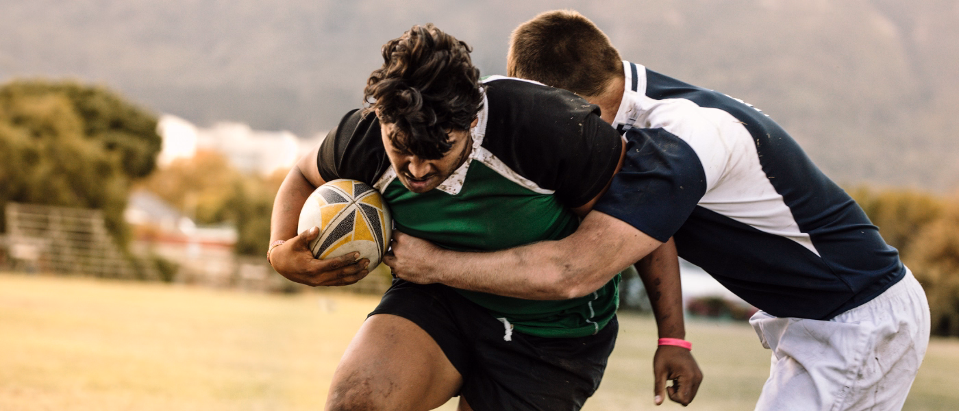Rugby player being tackled during a match, illustrating mechanical low back pain risk from heavy contact, spinal loading, and twisting forces in sports
