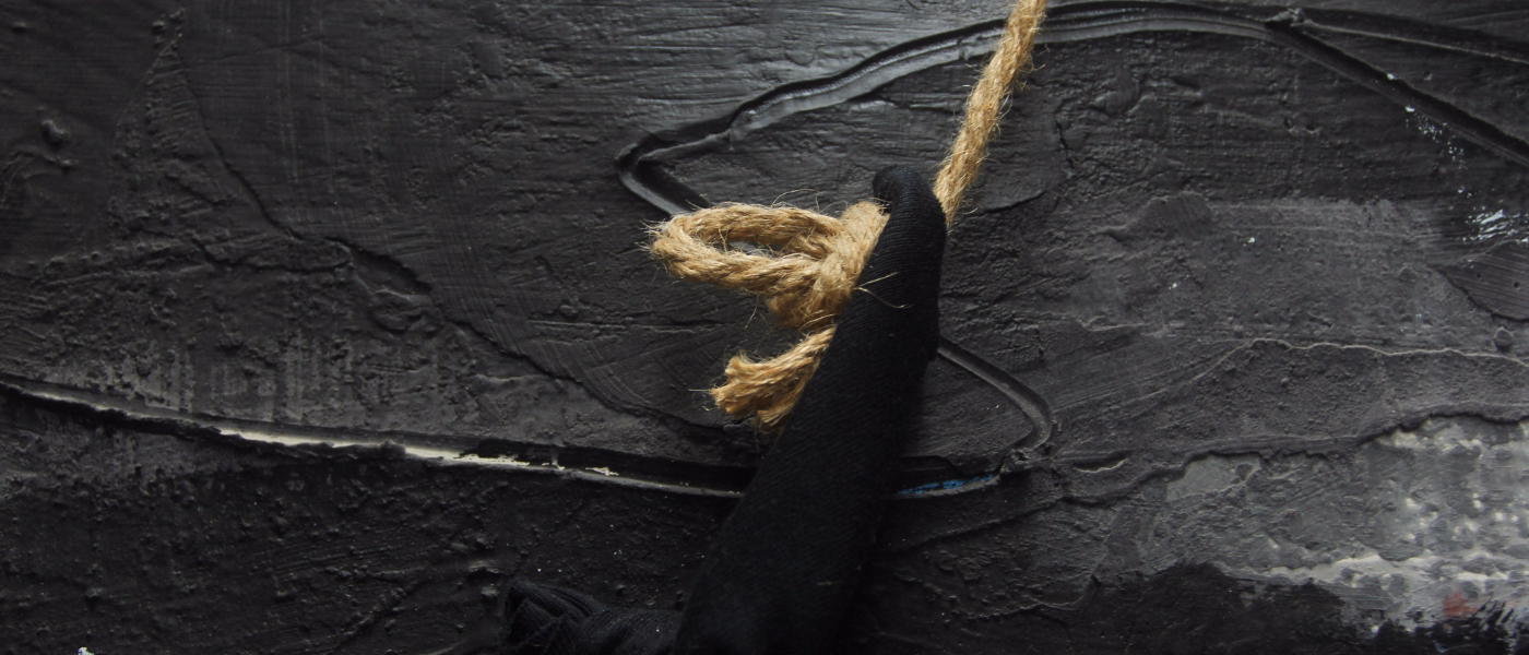 Taut rope cinched around black fabric on a dark textured wall, evoking the tight band-like pressure of a tension-type headache