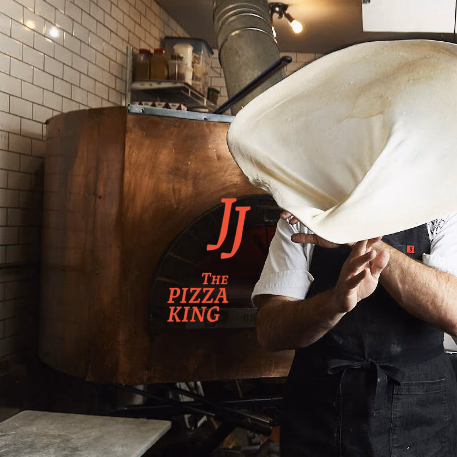 Chef tossing pizza dough in front of a large wooden pizza oven with JJ – The Pizza King logo.