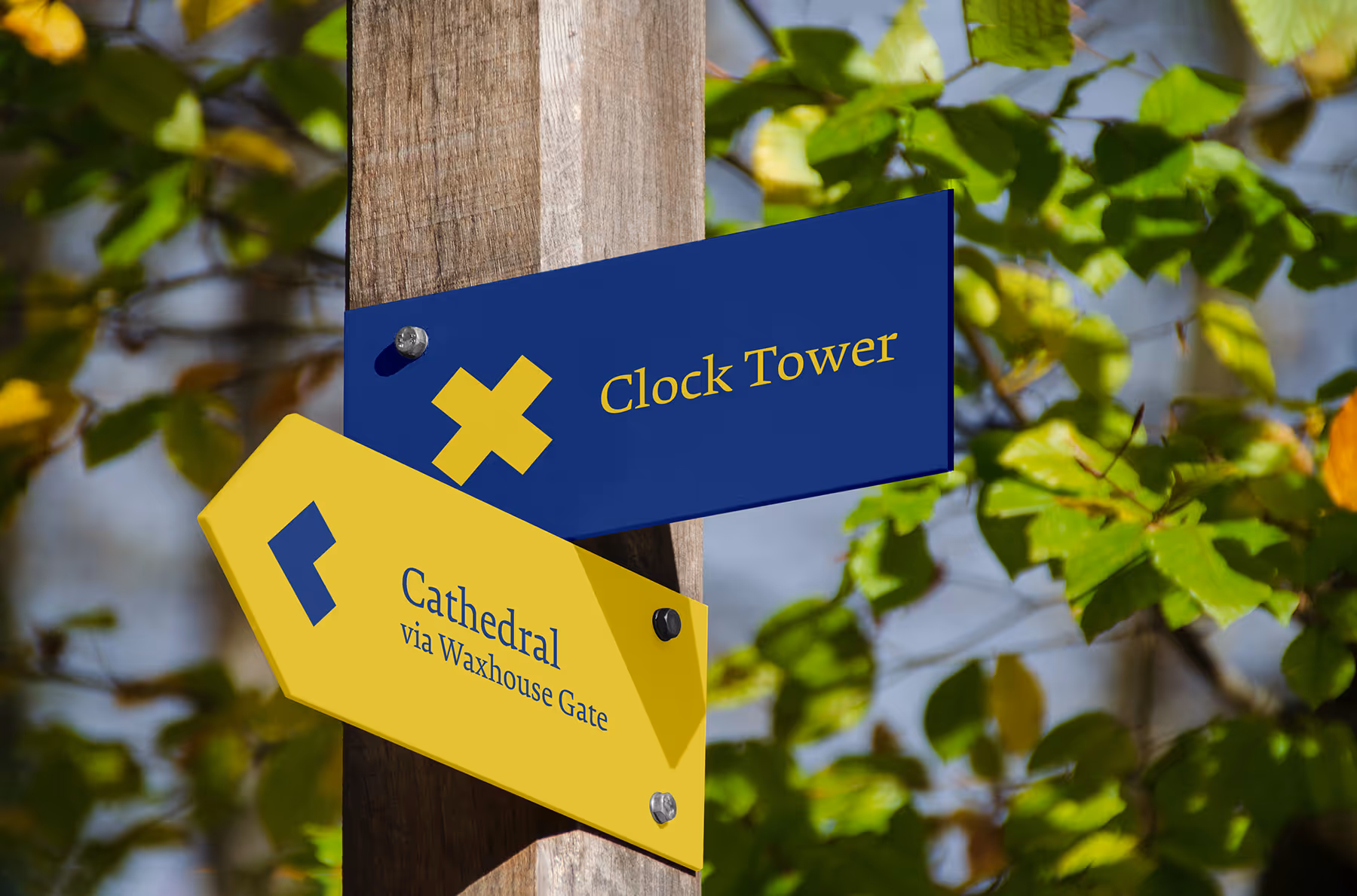 Wooden post with two directional signs: a blue one pointing to the Clock Tower and a yellow one pointing left to the Cathedral via Waxhouse Gate.