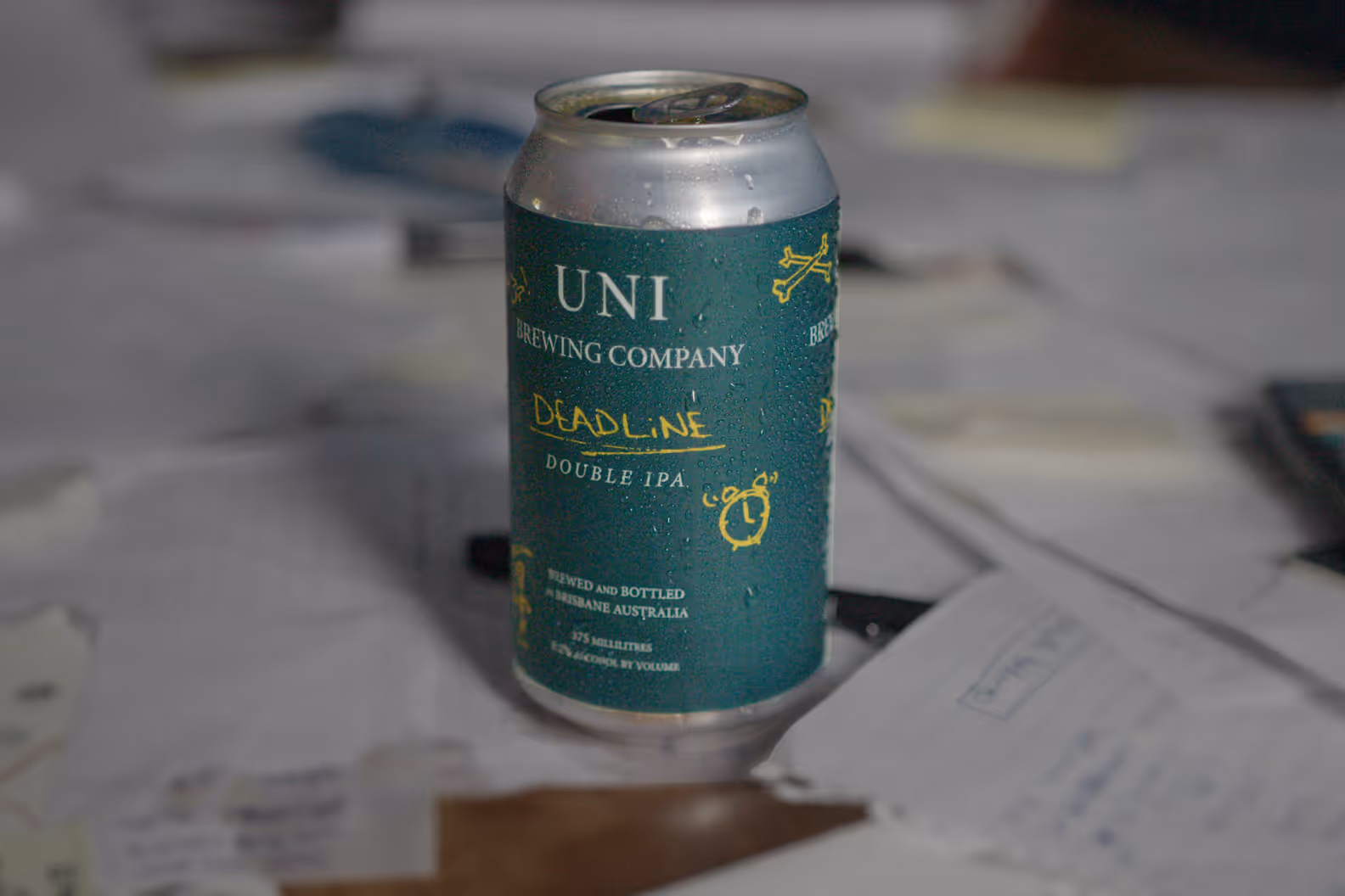 Condensation-covered can of Uni Brewing Company's deadline double IPA beer on a cluttered desk with papers and notes.