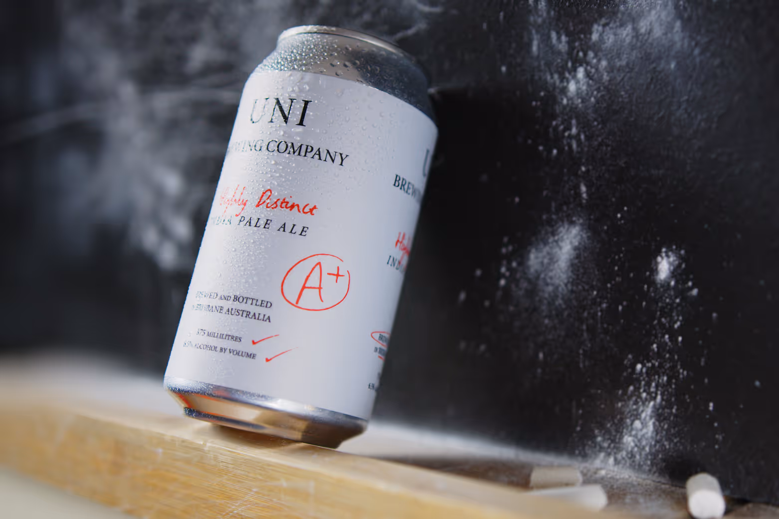 Condensation-covered can of Uni Brewing Company India Pale Ale balancing on a chalkboard with chalk dust and broken chalk pieces nearby.
