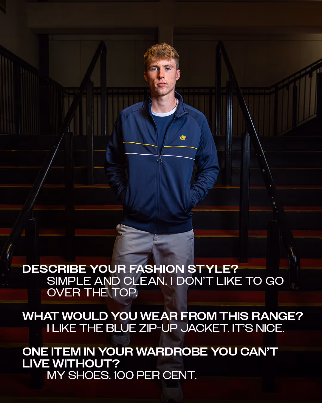 Conrad Hunt standing on dimly-lit stairs inside Vicarage Road stadium wearing a navy zip-up jacket and light pants with text overlay about fashion preferences and wardrobe essentials.