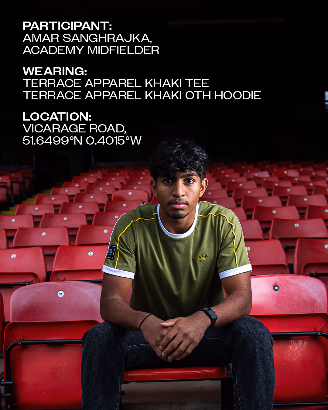 Amar Sanghrajka sitting in Vicarage Road stadium with red seats, wearing a khaki tee shirt with yellow details.