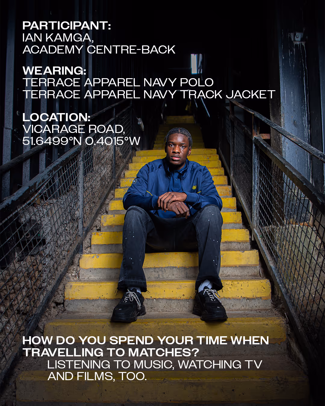 Ian Kamga sitting on yellow steps in a dimly lit stairwell at Vicarage Road stadium wearing a navy polo and track jacket.