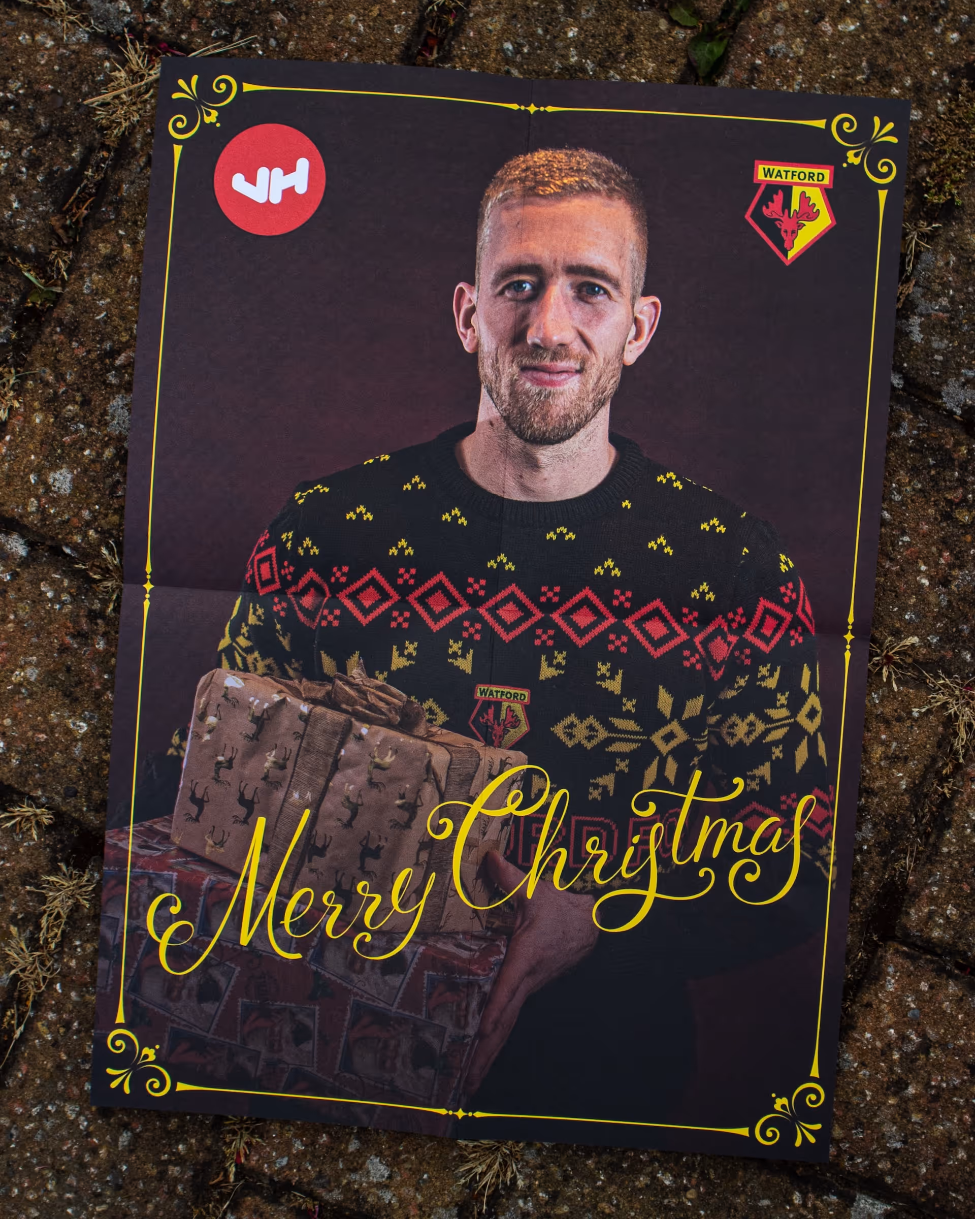 Watford football player Egil Selvik in a festive sweater holding wrapped Christmas gifts with 'Merry Christmas' text on the card.