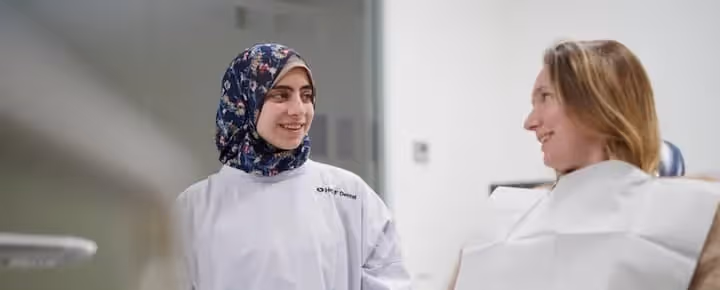 Two women smiling and talking in a dental clinic setting.
