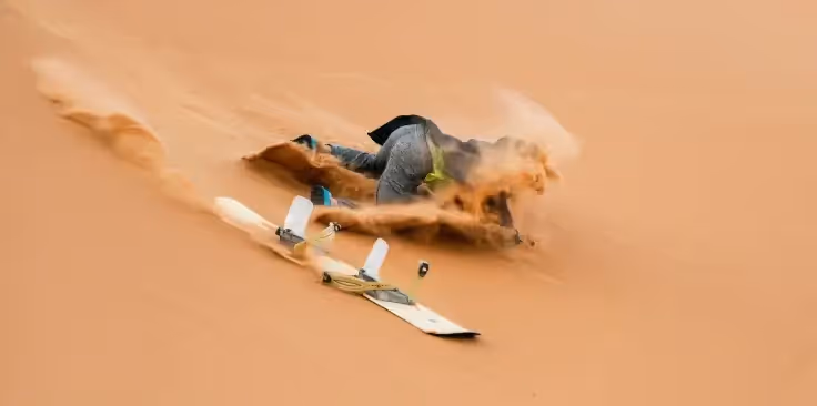 A person falling off of a snowboard in the sand