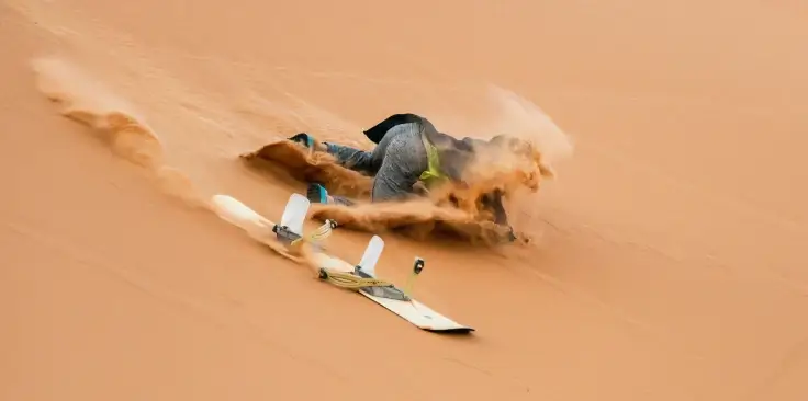 A person falling off of a snowboard in the sand