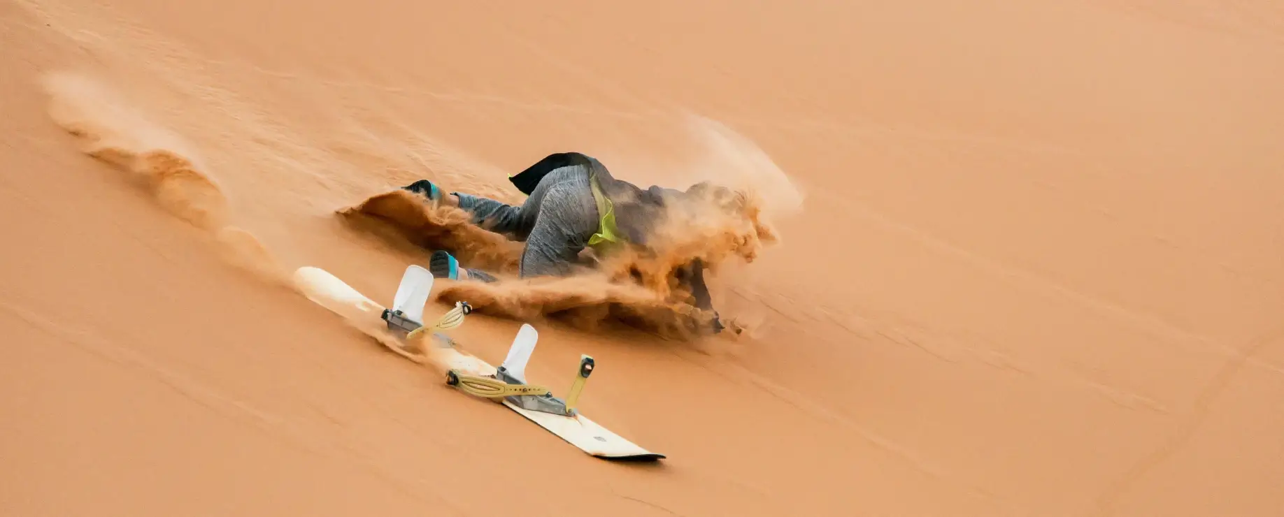 A person falling off of a snowboard in the sand