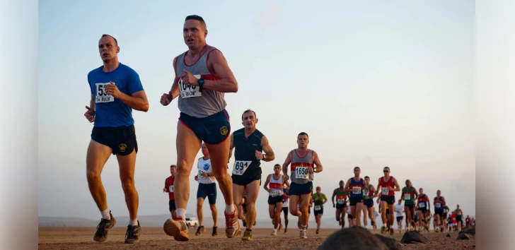A group of runners competing in a marathon on a dirt path, with a clear sky at what appears to be either dawn or dusk given the soft lighting. They are wearing various running bibs and athletic gear, suggesting a competitive event.