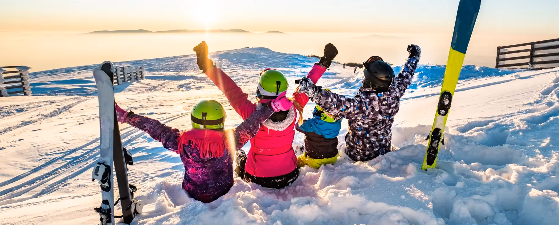 Group of skiers sitting in snow with arms raised at sunset.