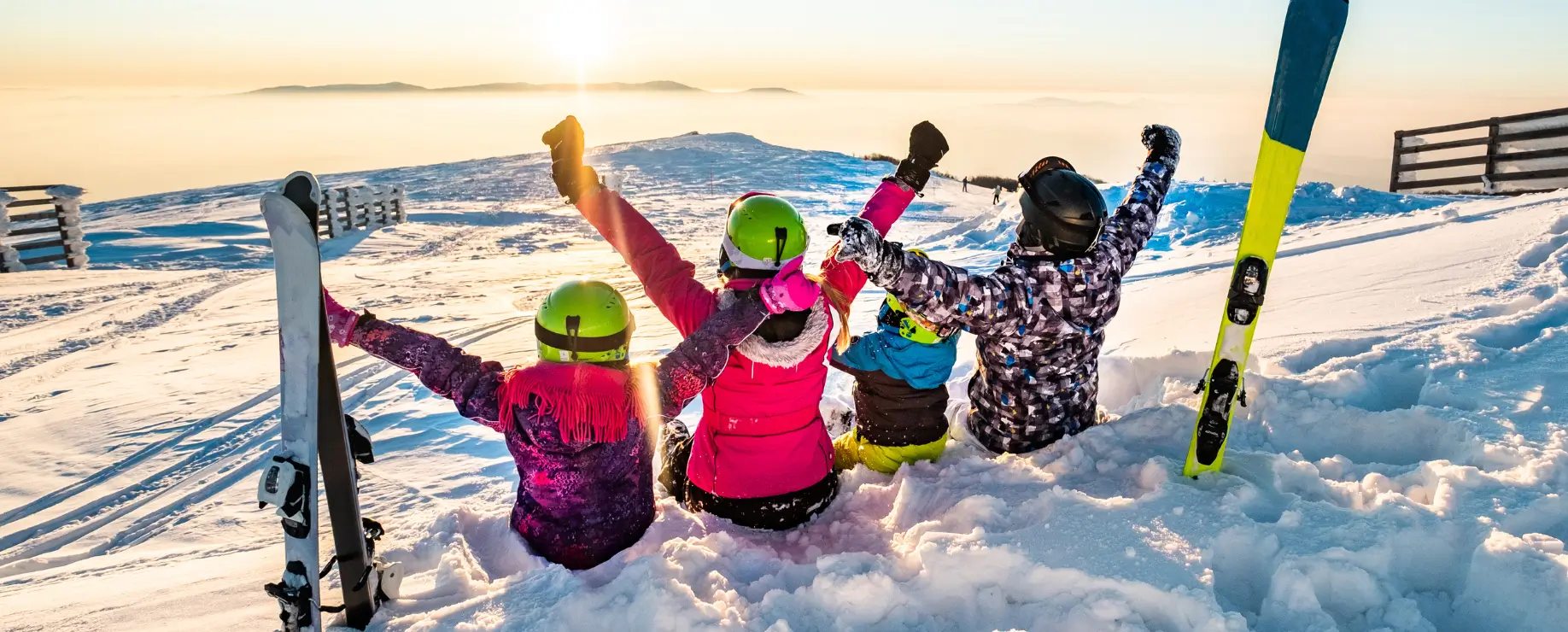 Group of skiers sitting in snow with arms raised at sunset.