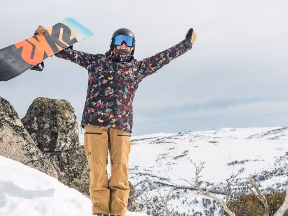 A Man Holding A Snowboard On Top Of A Snow Covered Mountain
