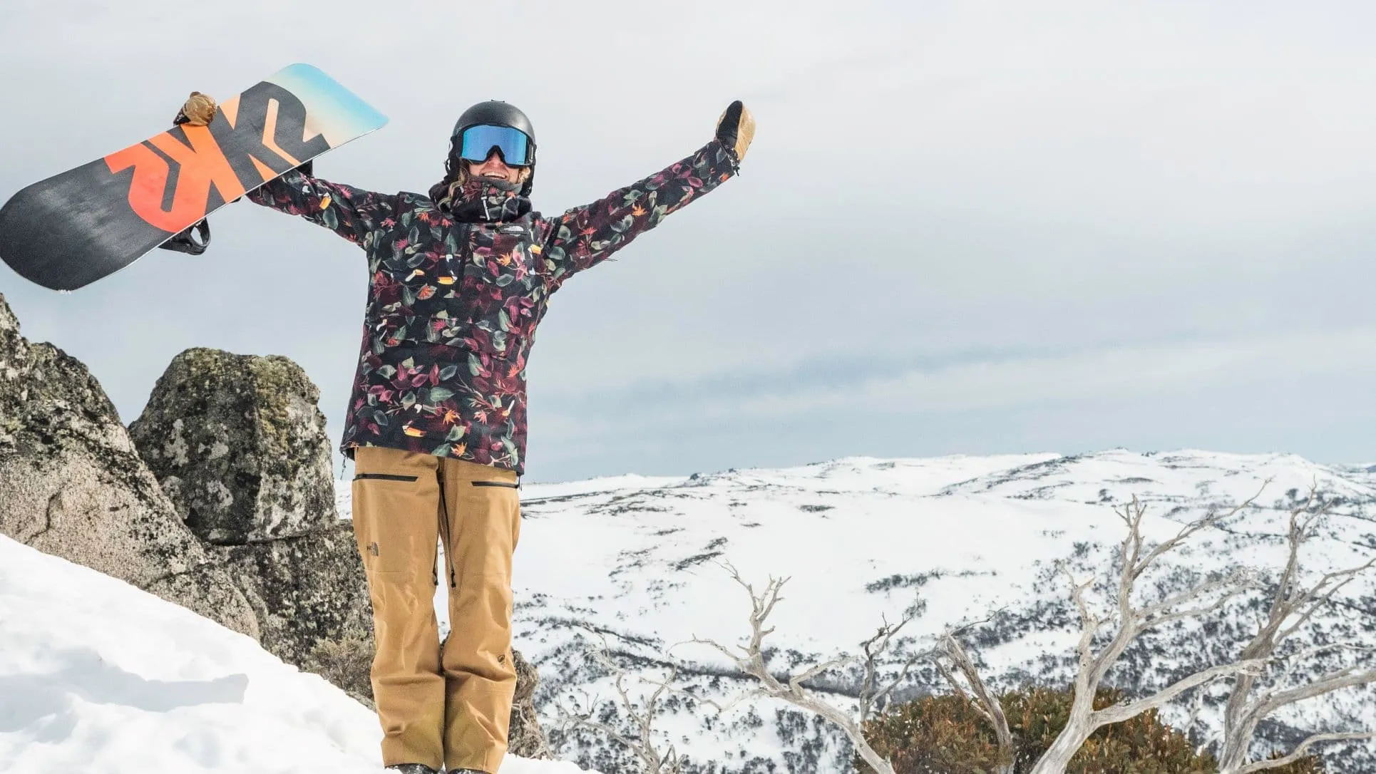 A Man Holding A Snowboard On Top Of A Snow Covered Mountain