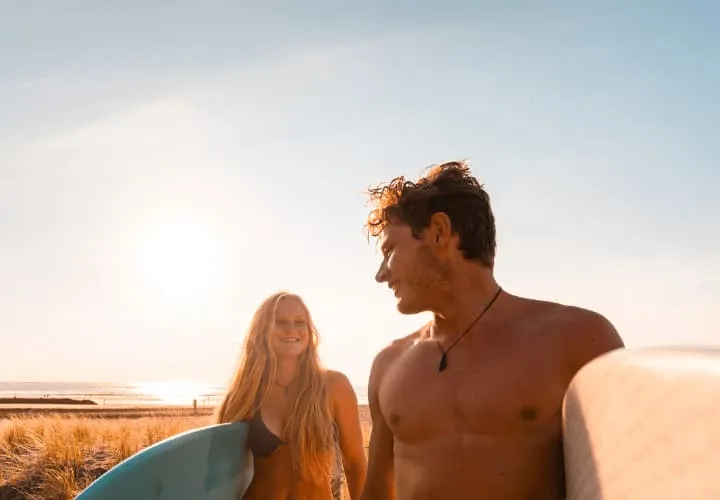 A Man And A Woman Holding Surfboards On A Beach