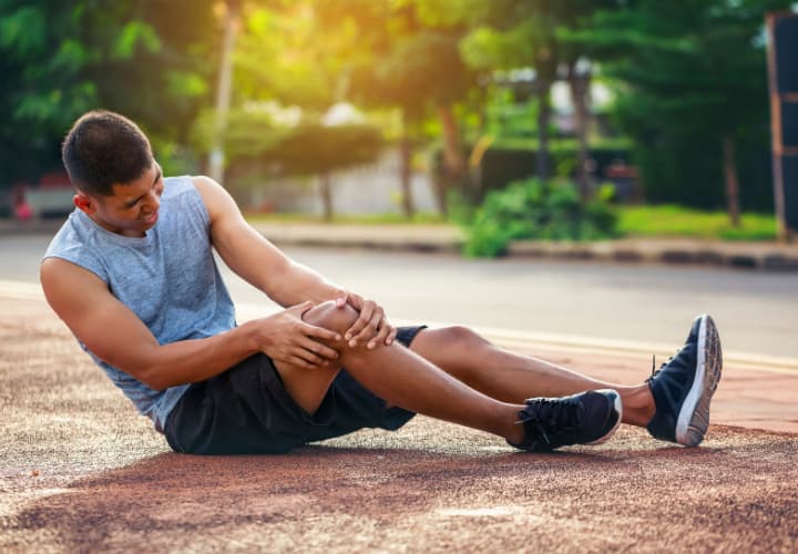 A Man Sitting On The Ground With His Knee In Pain