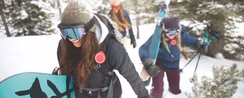 Women hiking in snow with skis and snowboards.