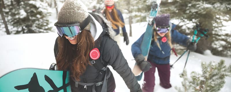 Women hiking in snow with skis and snowboards.