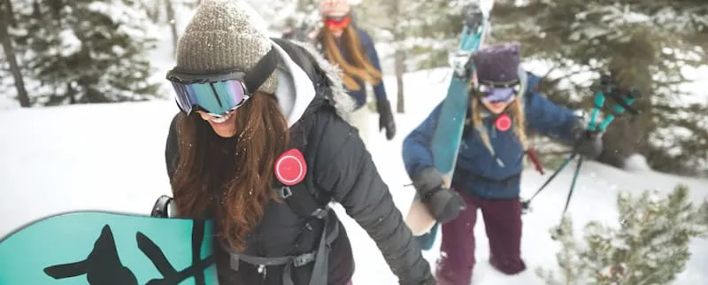 Women hiking in snow with skis and snowboards.