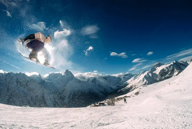 Snowboarder performing a mid-air trick on a snowy mountain slope with clear blue skies.