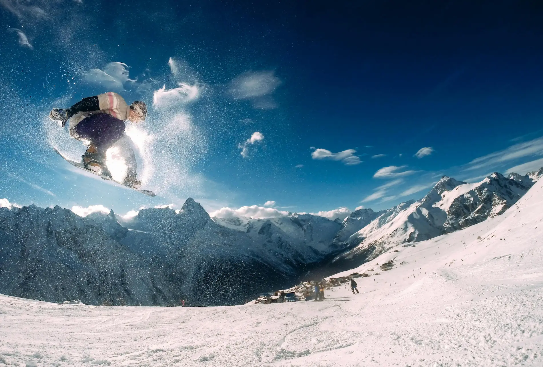 Snowboarder performing a mid-air trick on a snowy mountain slope with clear blue skies.