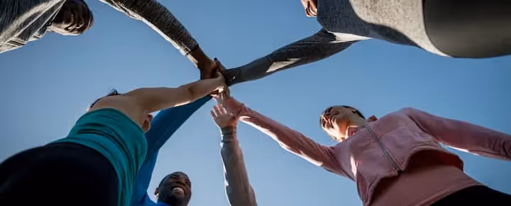 Group of people joining hands in a team huddle outdoors.